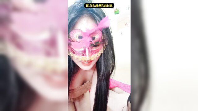 Asian beauty in pink mask and lingerie, teasing bare breasts closeup