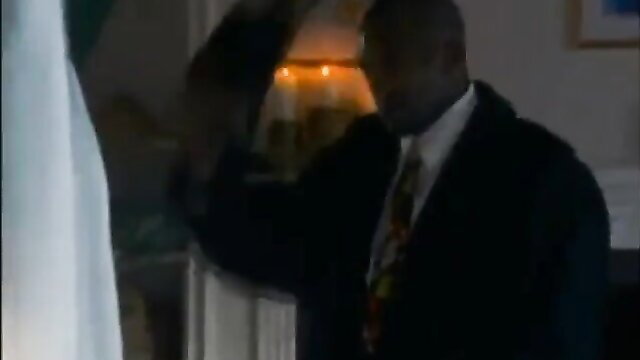 Black man in suit raising arm in dim-lit Passion Cove The Gift scene