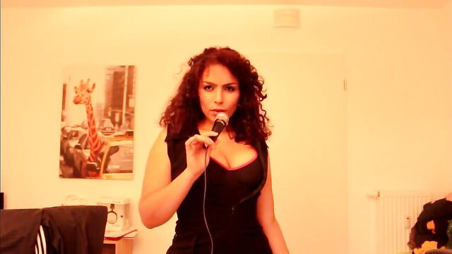 Curvy brunette in tight black dress holds mic, ASMR moaning sensual kisses