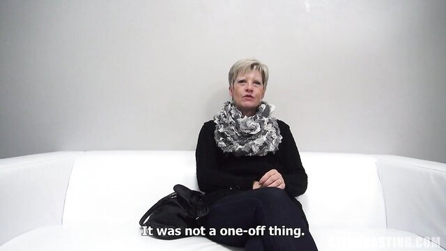 Mature blonde woman in scarf seated on couch at casting