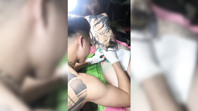 Asian tattoo artist inks full body tattoo on woman's thigh in Vietnam