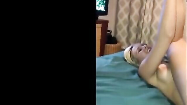 Blonde woman with towel on head lifts legs high on bed in explicit pose