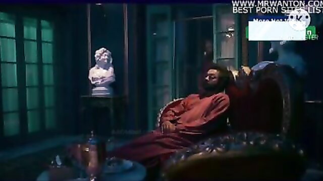 Bearded Indian man in red robe lounging seductively in Ashram web series sex scene
