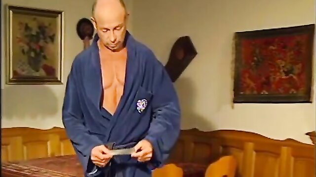 Bald muscular man in open blue robe holding knife, Herzog adult video thumbnail