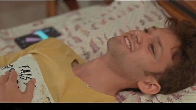 Smiling Indian guy in yellow shirt lying on bed, phone nearby