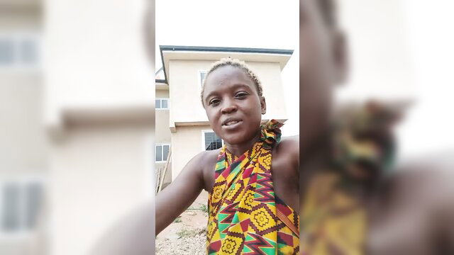 Ghanaian woman in colorful tribal dress, smiling selfie outdoors