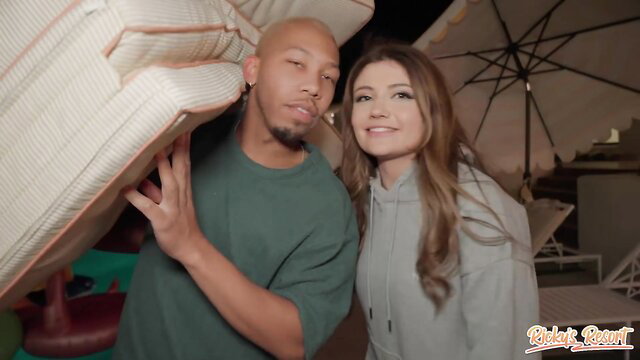 Bald Black guy and smiling brunette posing with mattress at Ricky's Resort