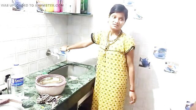 Indian housewife in yellow nightie washing dishes in kitchen