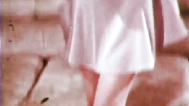Retro blonde in sheer pink babydoll dress teases legs on couch