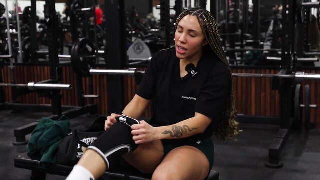 Mixed athlete with braids adjusting thick thighs knee sleeve gym leg day