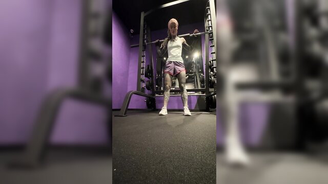 Anuskatzz tattooed fit girl squatting in gym, pink shorts tank top