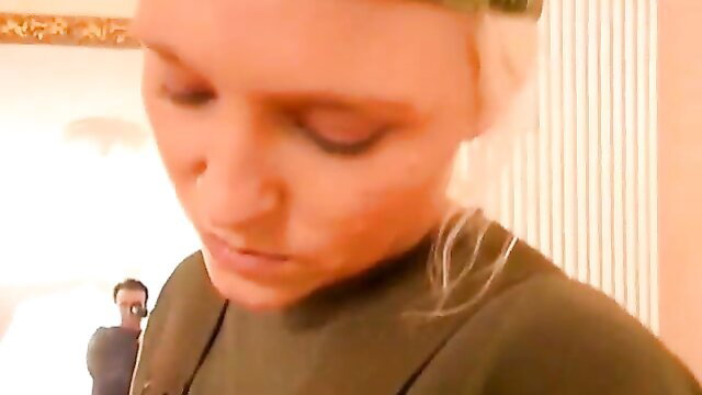 Blonde woman in green top looks down at man filming in lesbian slave sex clip