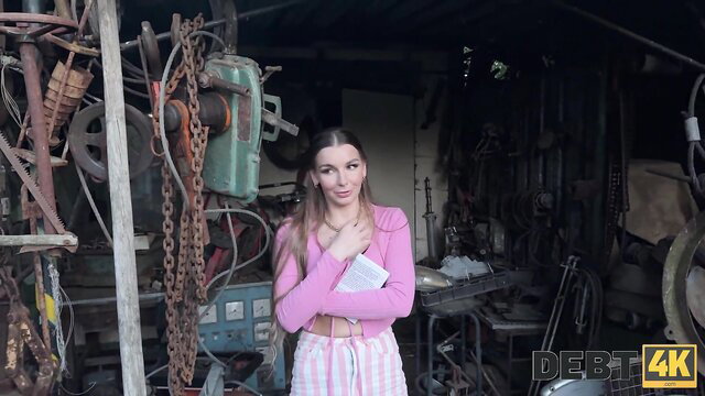 Arina Shy in pink sweater and pants holding book in gritty garage