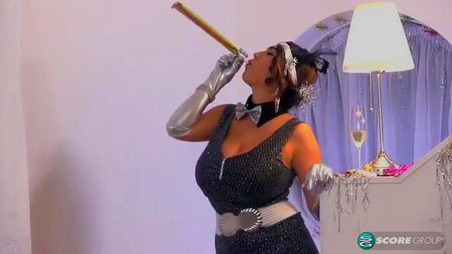 Curvy brunette in sparkly black flapper dress blows party horn for Happy Boob Year