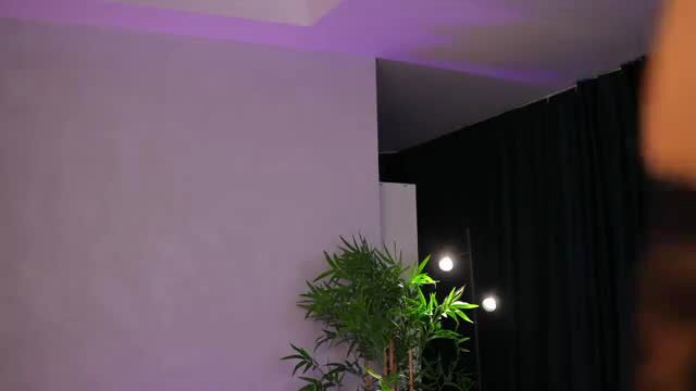 Kiss Jess in purple-lit room with plants, seductive pose