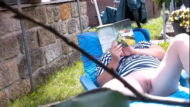 Mature woman in striped outfit reading on lounge chair outdoors