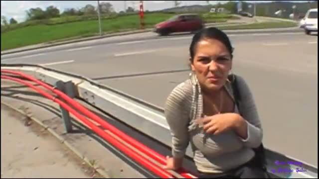 Brunette woman with large breasts sitting on roadside guardrail