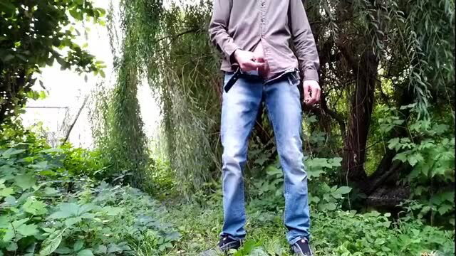 Man in jeans adjusts pants while standing outdoors in park
