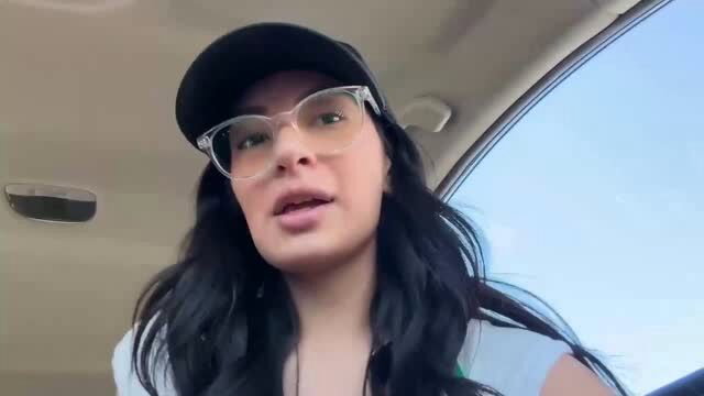 Brunette woman in glasses and black cap talking in car selfie video