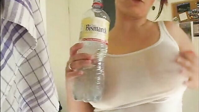 Busty brunette in wet white tank top holding Bismarck water bottle, see-through tits