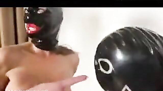 Shemale in latex mask points at blow-up doll in titslapping fetish thumbnail
