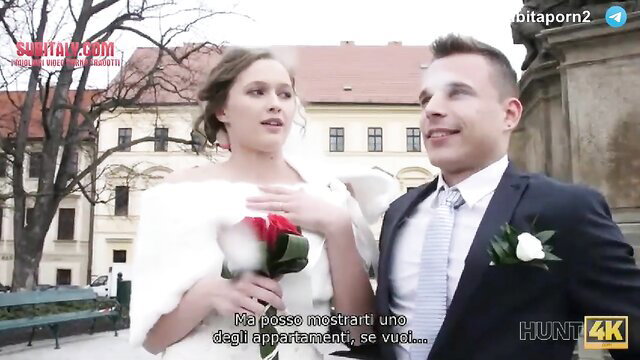 Newlywed brunette bride in white fur stole flirts with suited man outdoors