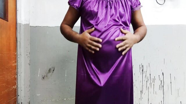 Pregnant man in purple nightdress cradling huge belly, seductive pose