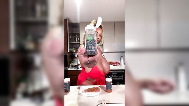 Persephanii in red bikini holds spice jar over kebab plate in kitchen