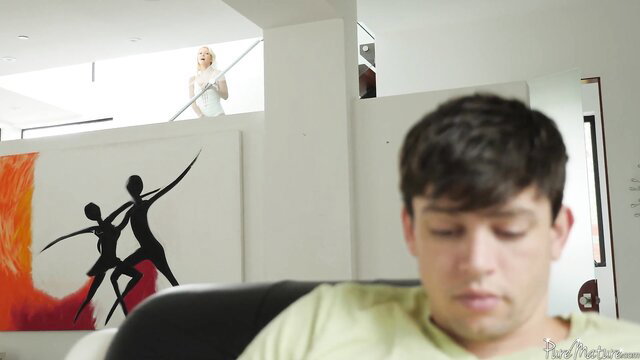 Horny lonely blonde stepmom in white dress overlooking guy on couch
