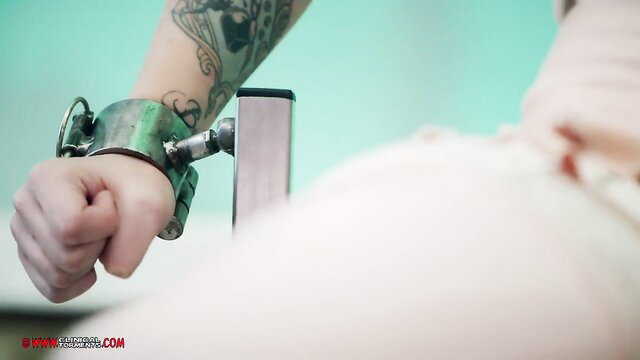 Tattooed woman in green metal handcuffs locked to metal bar, BDSM restraint