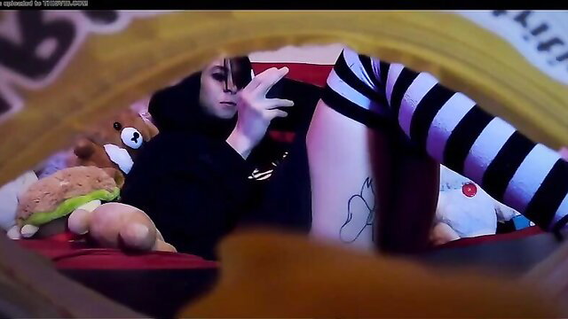 Pale goth gamer girl in striped stockings poses with plushies on bed