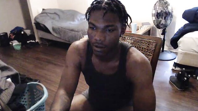Muscular black guy with braids sits in tank top and shorts, intense stare