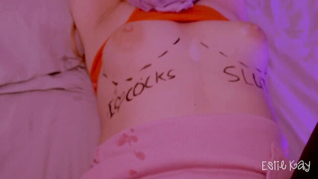 Estie Kay's tits marked 'I love cocks slut' in pink lingerie