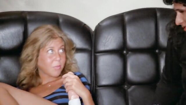 Blonde with big tits holds dildo, chats intimately with man on couch in 1979 Raunchy Heights