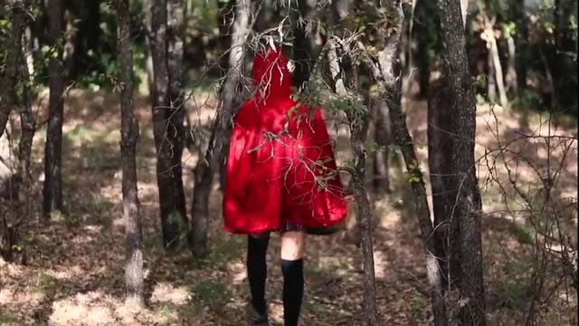 Person in red cloak and black stockings standing in forest woods