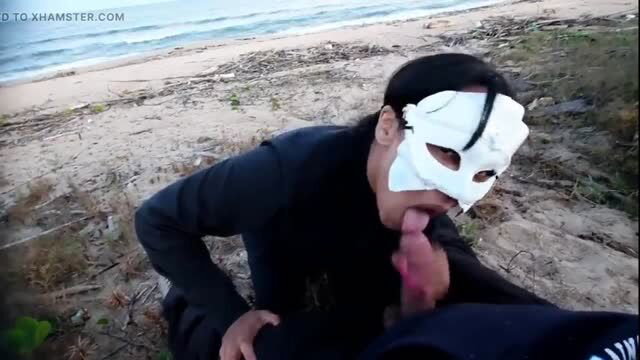 Masked man in black performs oral sex on beach