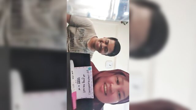 Malay couple selfie with plane ticket, smiling man and hijab woman