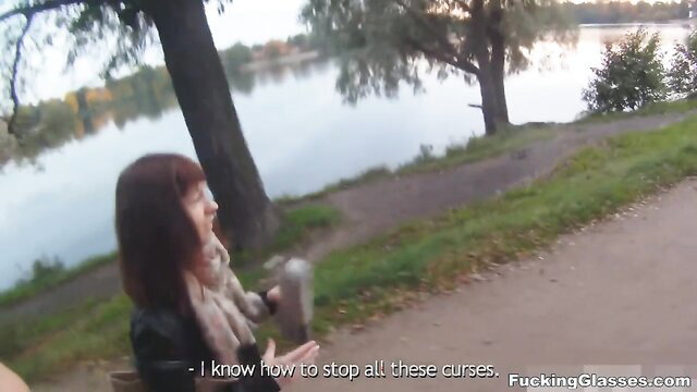 Redhead coed with glasses smiles outdoors by lake in orgy park tease