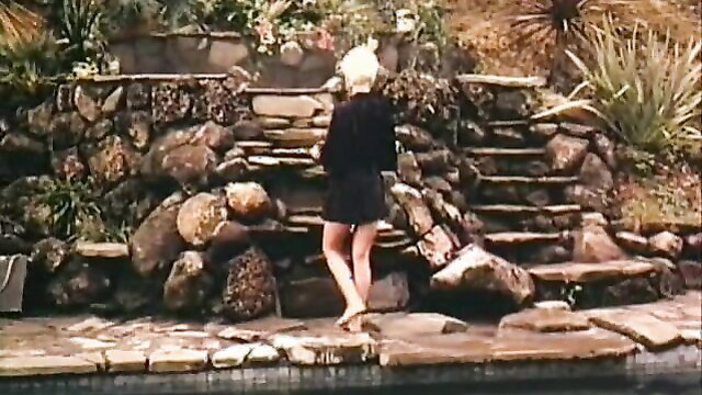 Blonde short-haired retro babe in black mini dress on rocky steps by pool