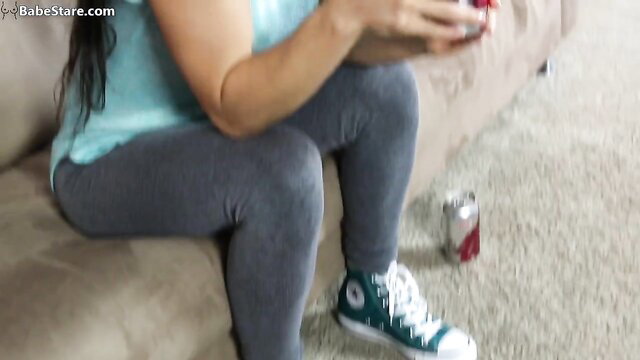Tia Will in tight top and gray leggings holding phone, burping fetish tease