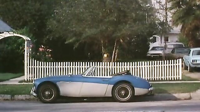 Retro blue Austin Healey sports car parked by white picket fence