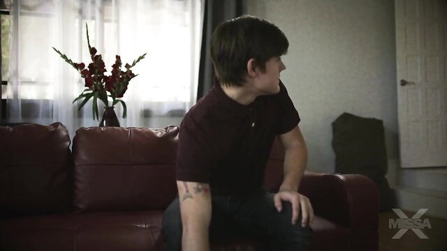 Syren De Mer lounging on couch in maroon polo shirt, tattooed arm