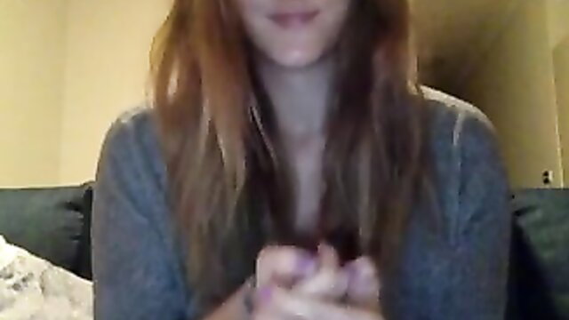 Sweet redhead cam girl smiling, hands clasped over gray sweater cleavage