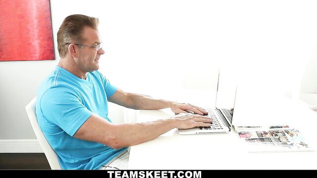 Older man in blue tee typing on laptop at desk