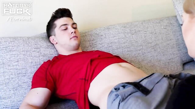 Hot young stud in red shirt and gray pants lies on couch showing abs