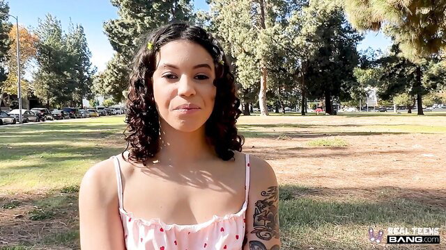 Cute mixed teen Nico Luva in pink cami top smiling outdoors park
