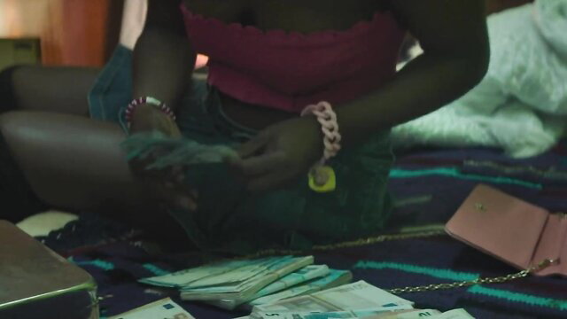 Yolanda Sey counting thick stacks of cash on bed in tight top and shorts