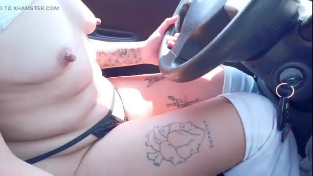 Naked tattooed woman driving car with steering wheel and visible tattoos