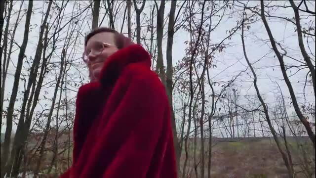 Woman in red fur coat outdoors by trees near highway