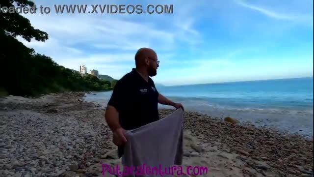 Bald man in black shirt holding grey towel on pebble beach